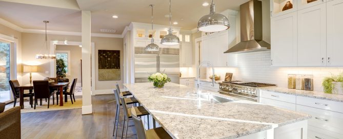 White kitchen design features large bar style kitchen island with granite countertop illuminated by modern pendant lights. Northwest USA