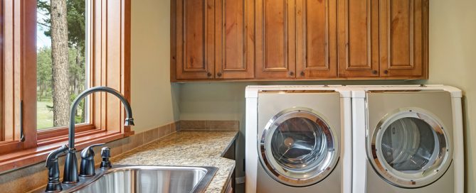 Huge laundry room with white washer and dryer, brown wood cabinets, granite countertop framing the sink with black faucet. Northwest, USA