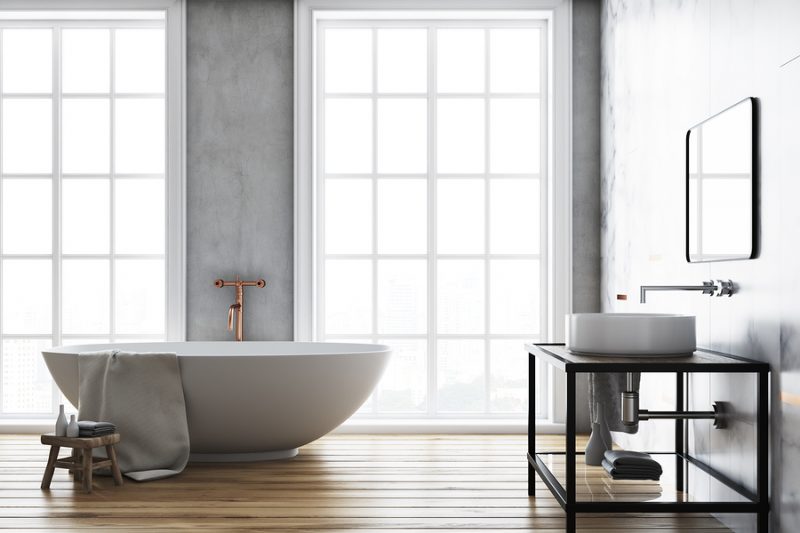 Luxury bathroom interior idea. A wooden floor, a large window and a white bathtub and sink. Concrete walls. 3d rendering mock up